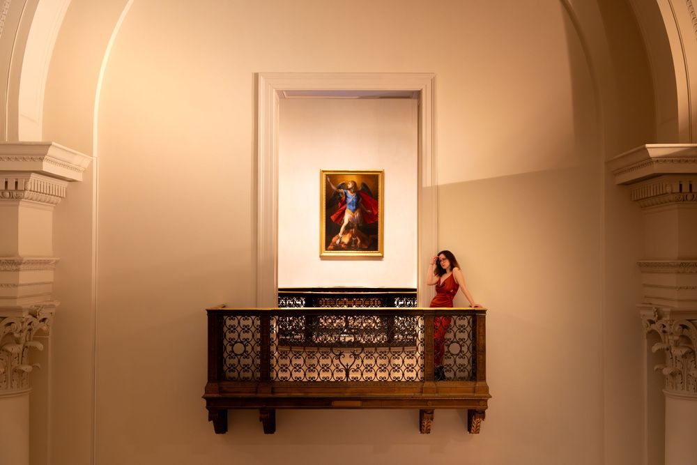 Ornate interior of a historic church with white walls, decorative moldings, and framed artwork mounted high on the walls.