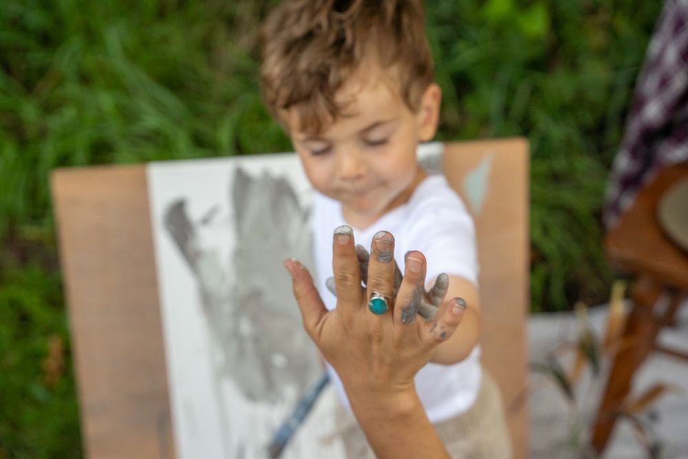 A child shows their paint-covered hand while working on an art project outdoors.