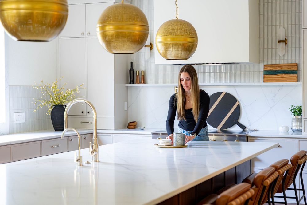 Modern kitchen interior with white cabinets, brass pendant lights, and a long marble island with wooden barstools.