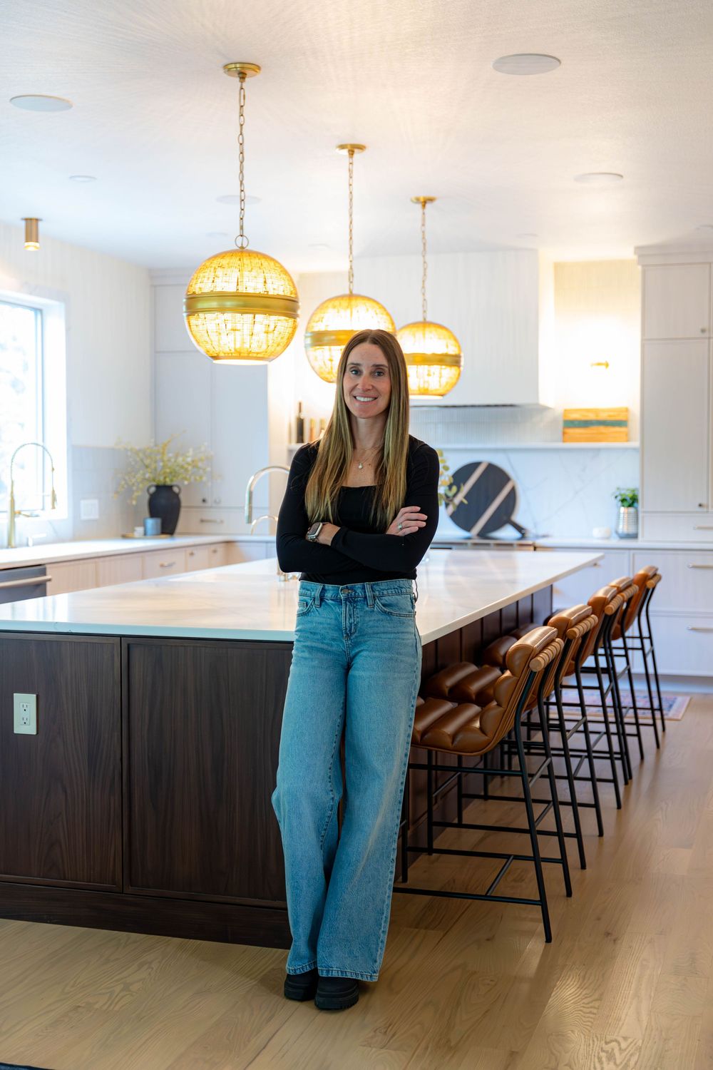 Modern white kitchen features yellow pendant lights, dark wood base cabinets, and bar seating with hardwood flooring.