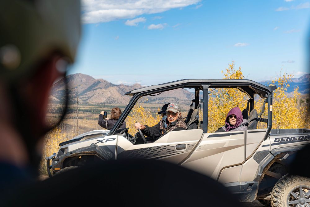 Off-road vehicle with passengers enjoying a scenic mountain drive with autumn foliage and blue skies in the background.