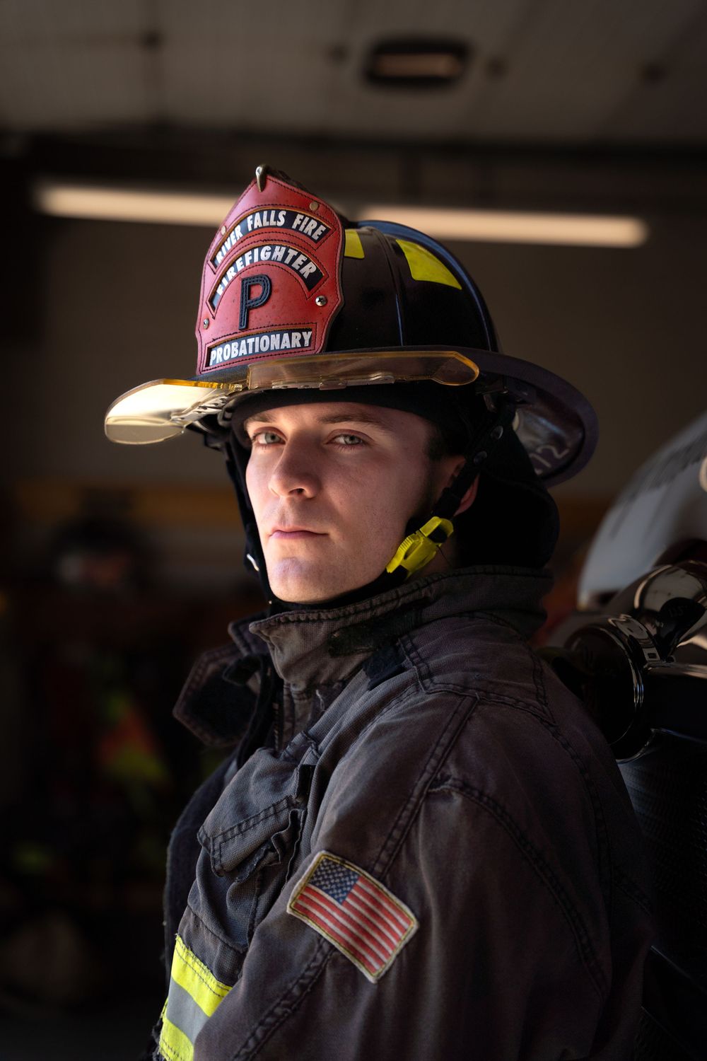 A firefighter in protective gear wearing a pink helmet with reflective stripes against a dark background.