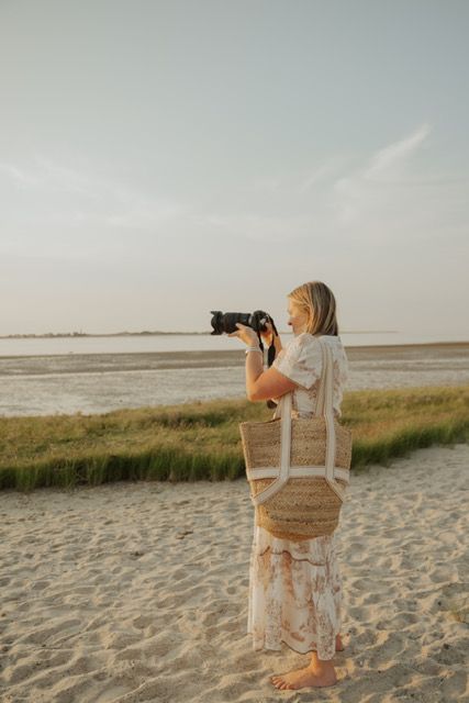 Female photographer shooting with DSLR camera on sandy beach at sunset.