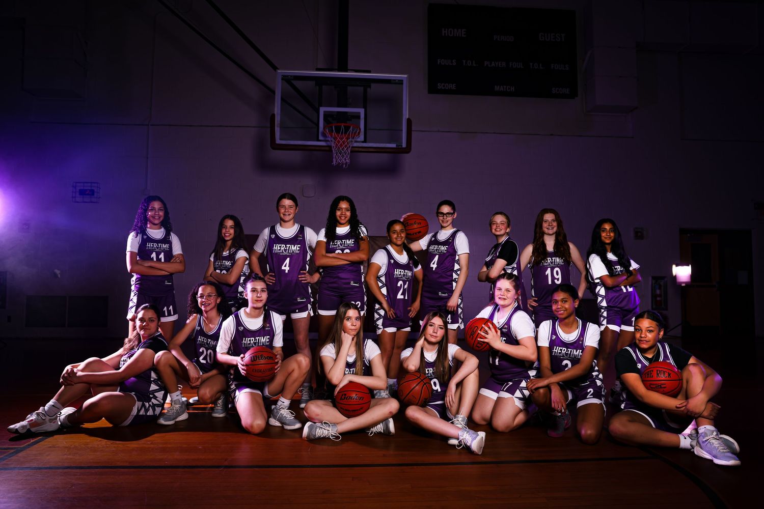Group of female athletes pose together on tennis court for team photo.