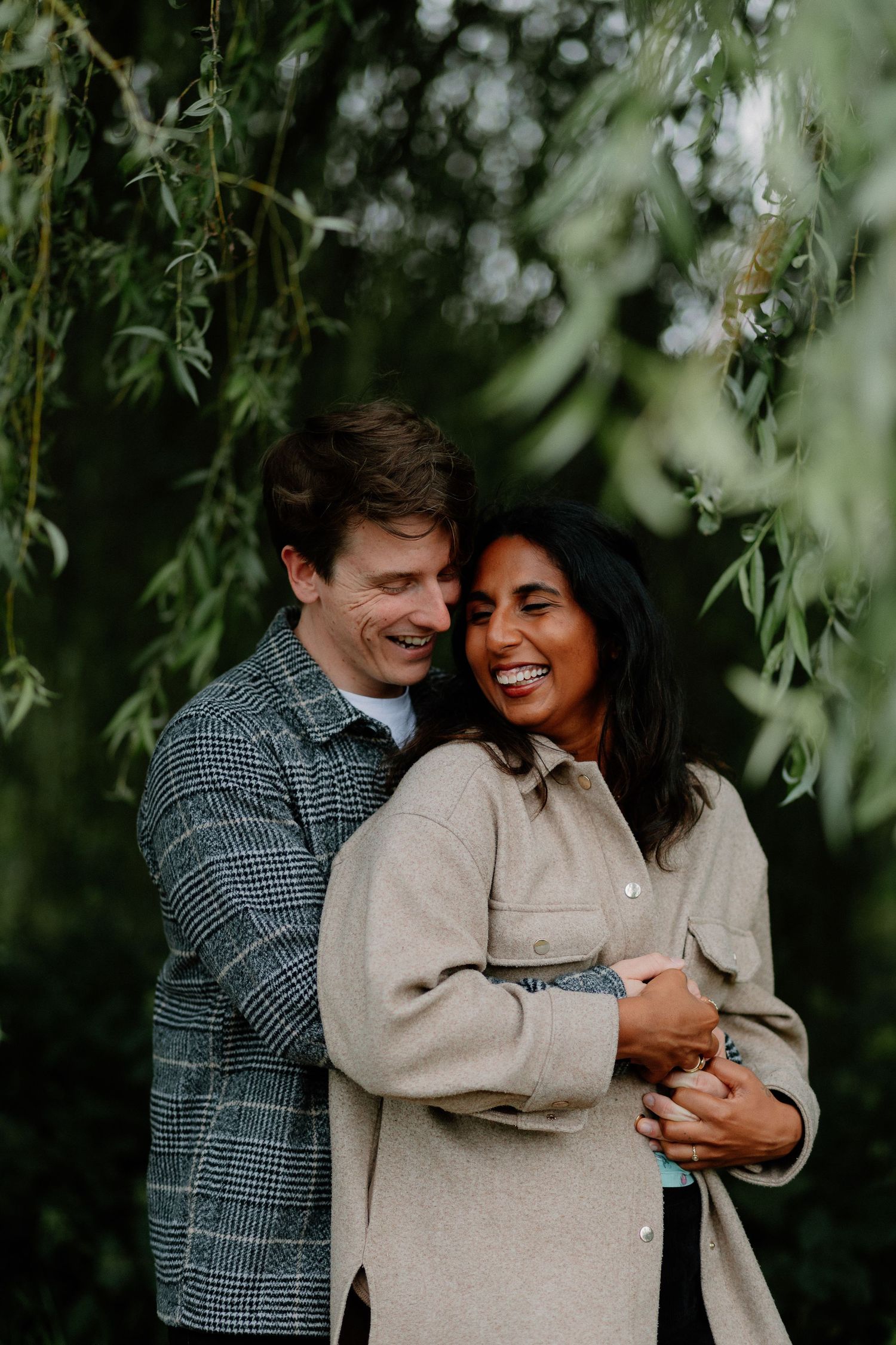 Couple sharing intimate moment under weeping willow tree branches.