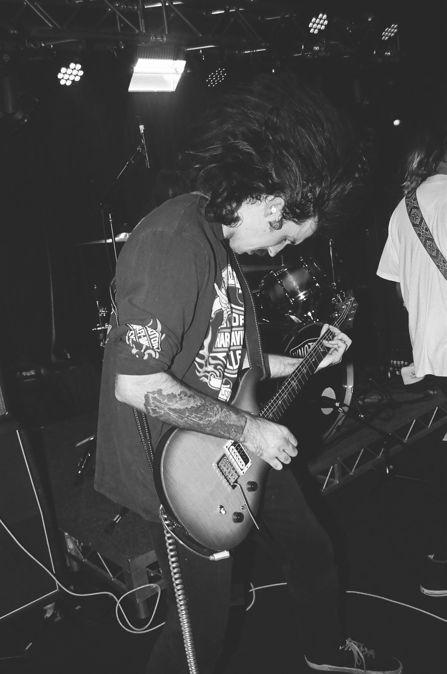 Guitar player with tattooed arm performing energetically on dimly lit stage.