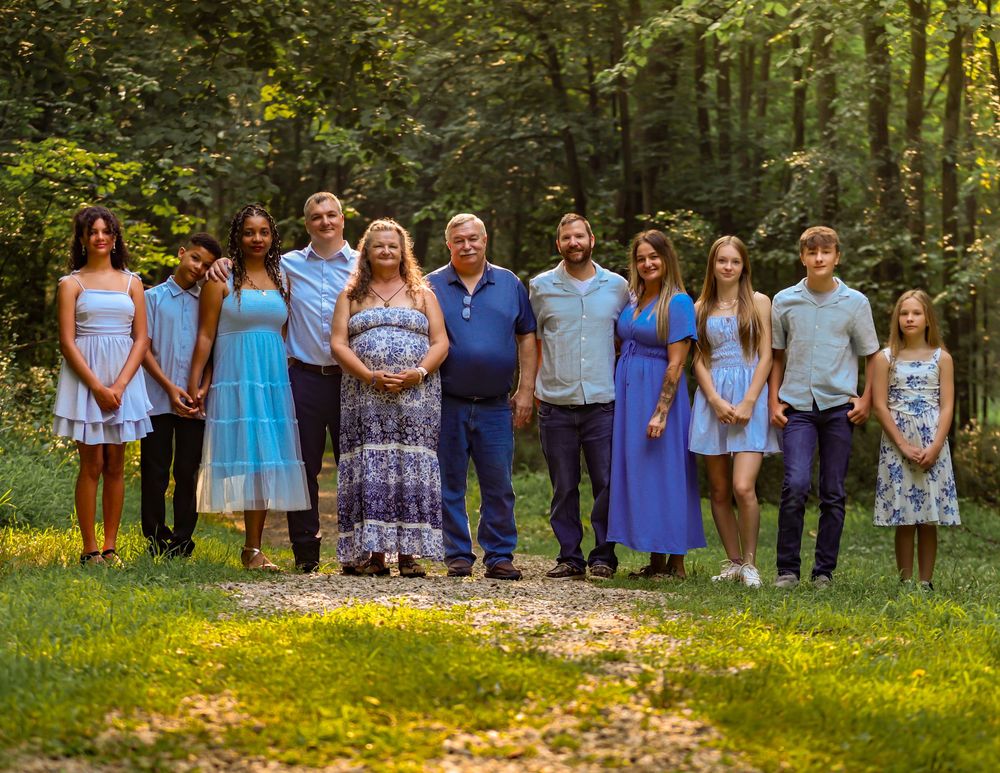 Large family group dressed in coordinating blue and white outfits poses together for outdoor photos in nature setting.