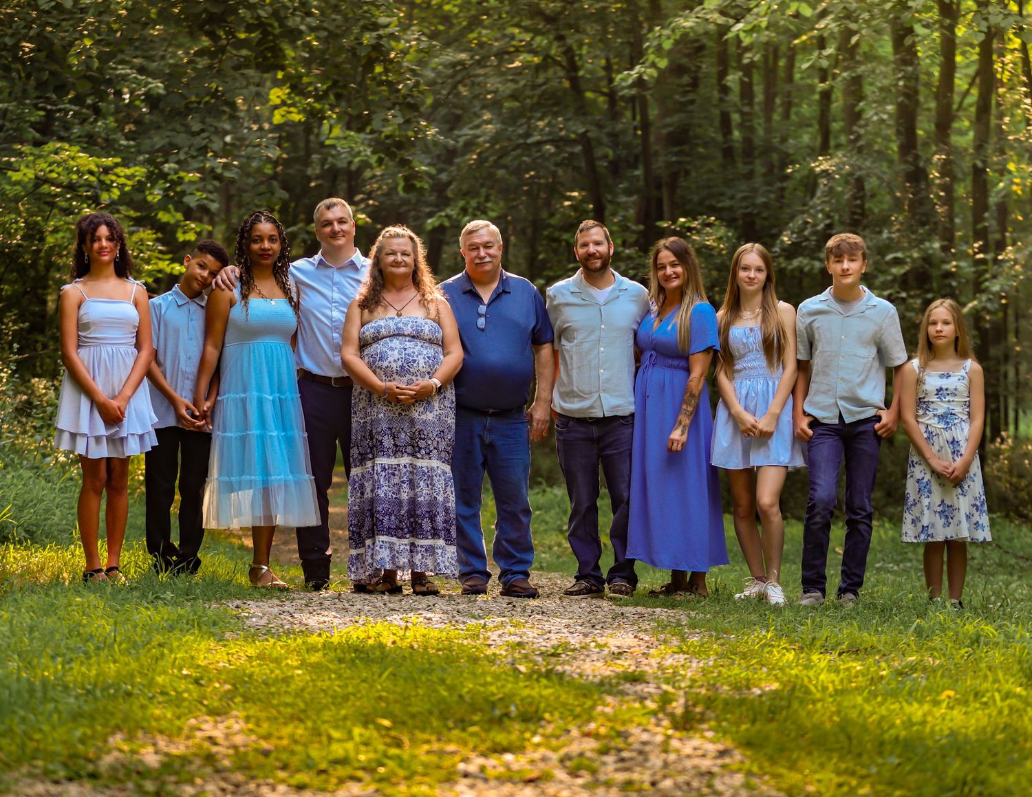 Large family group dressed in coordinating blue and white outfits poses together for outdoor photos in nature setting.
