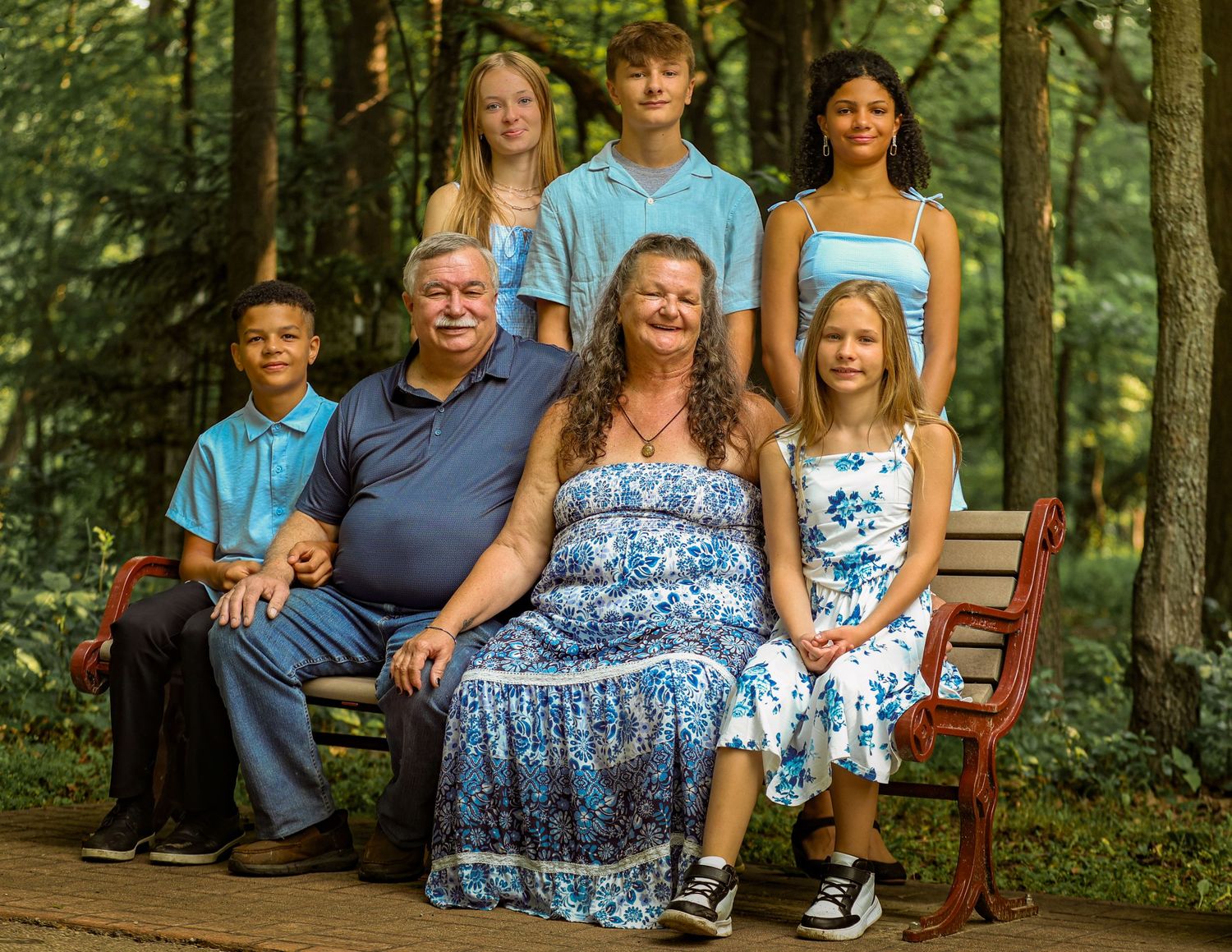 A family poses together outdoors in coordinated blue outfits against a lush forest backdrop.