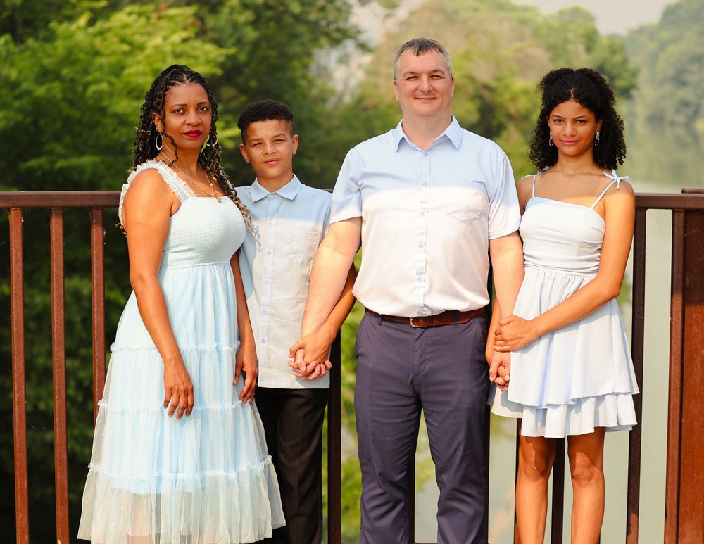 Family members dressed in coordinating blue and white outfits pose together on an outdoor deck for a portrait session.