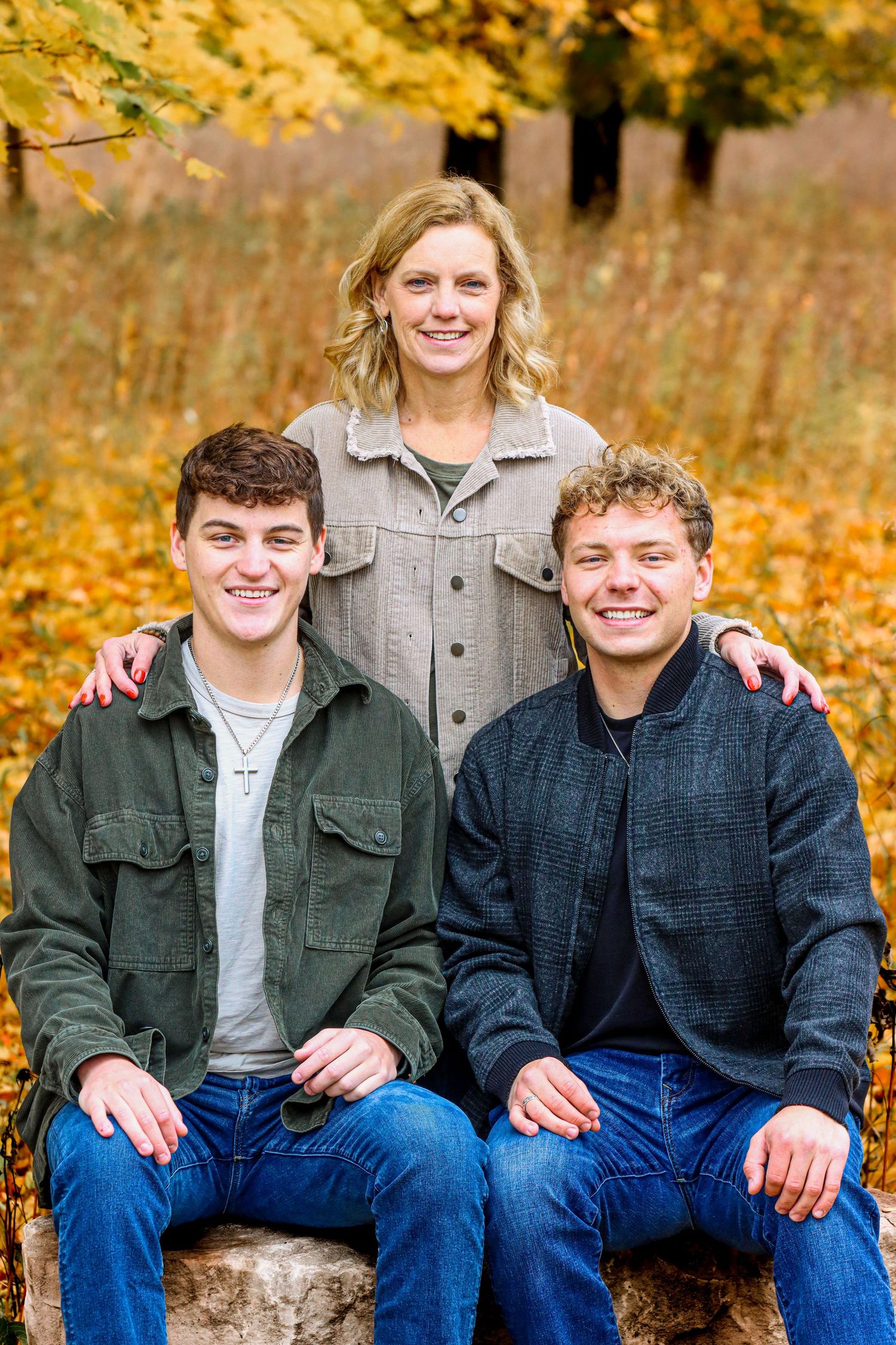 Three people pose together on bench with vibrant autumn foliage in background.