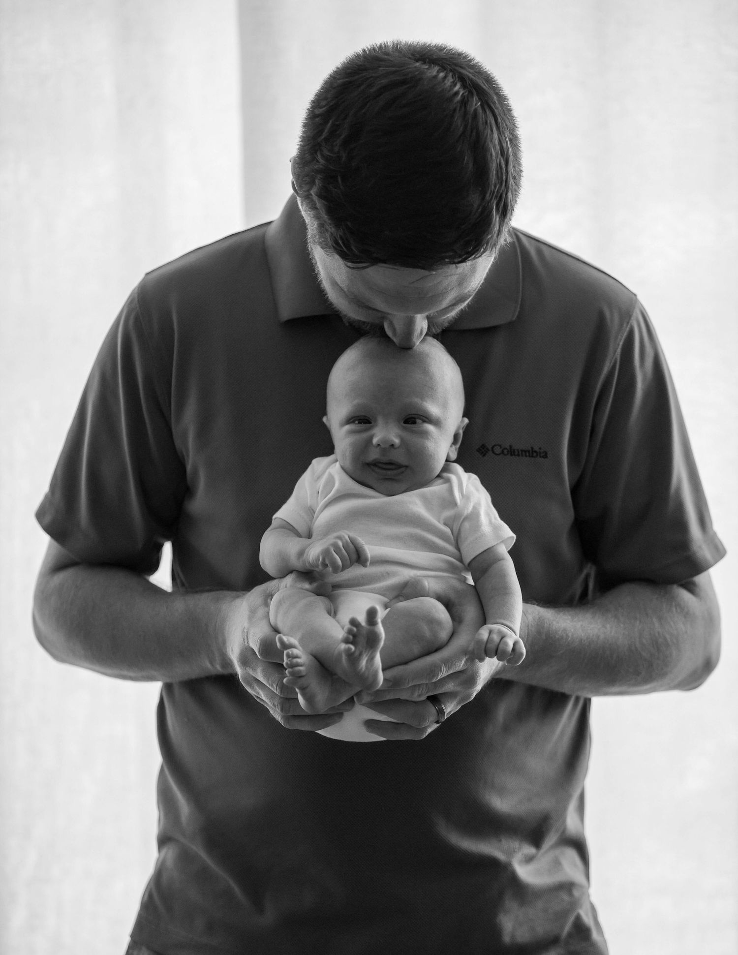 Tender moment captured in black and white as a person in a polo shirt holds and kisses a small baby.