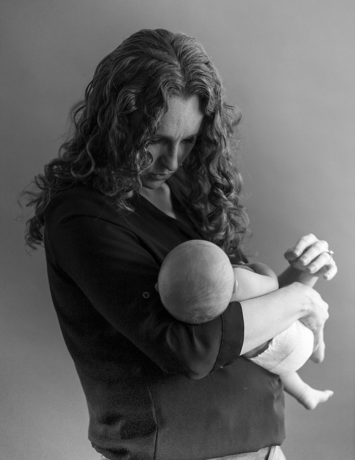 Black and white portrait of someone with curly hair holding and gazing down at an infant.