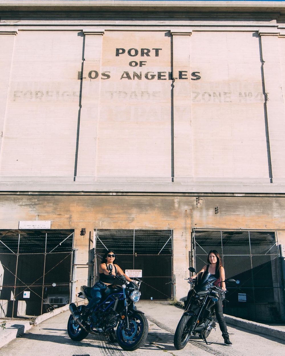 A row of motorcycles parked in front of an industrial building with white walls and signage.