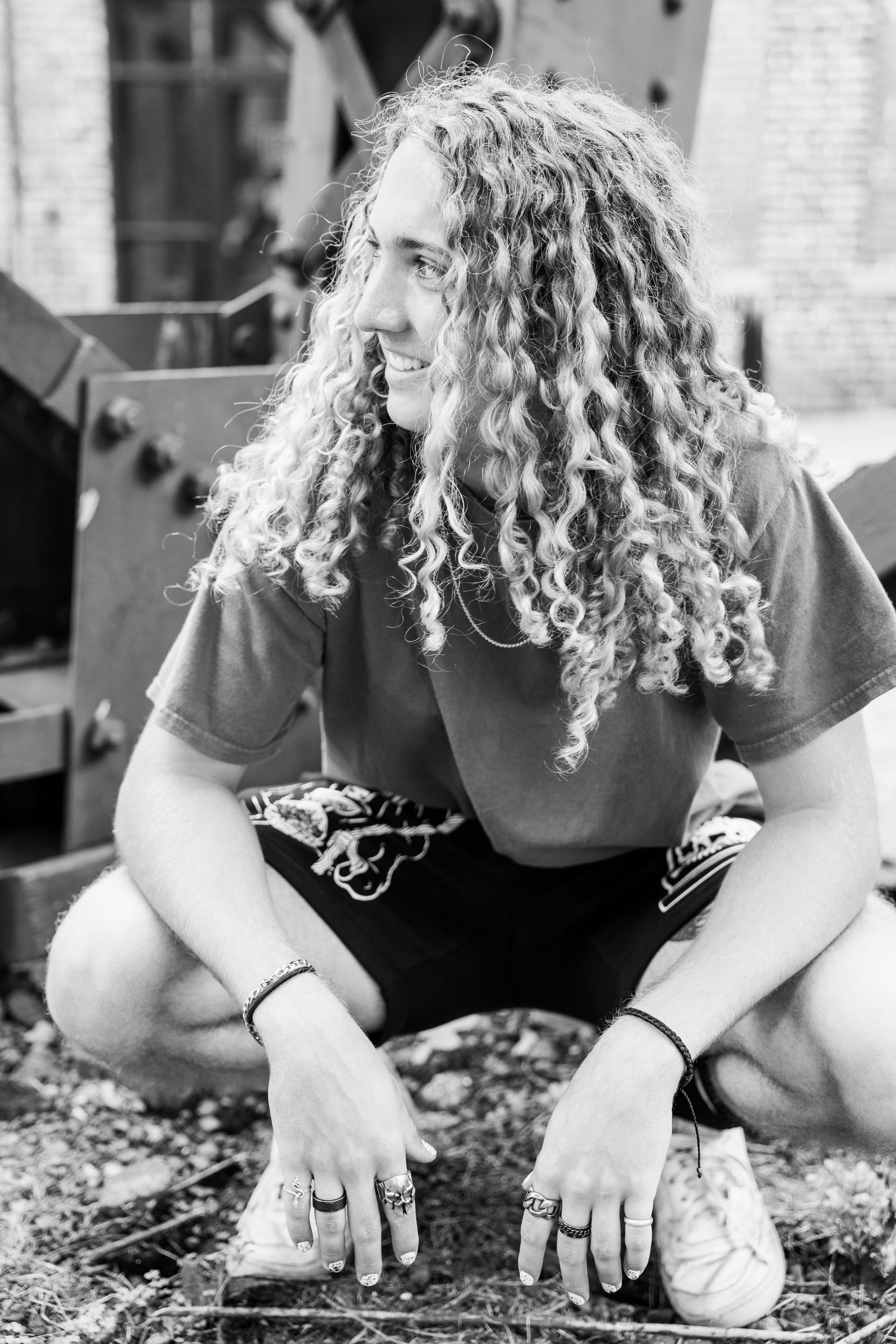 Black and white portrait of someone with long curly hair crouching in casual attire.