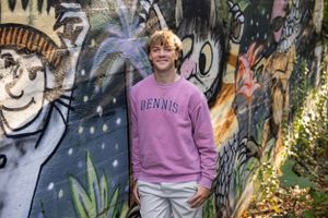 Person wearing pink sweatshirt standing in front of colorful graffiti wall.