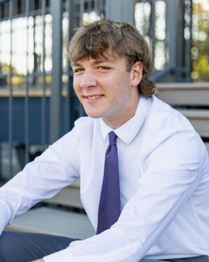 Student in white dress shirt and purple tie posing outdoors.