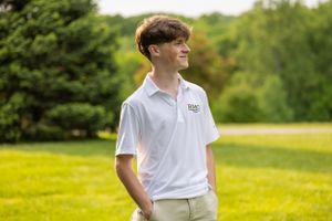 Students in white polo uniforms photographed outdoors on sunny day.