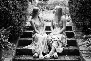 Two people in floral dresses sit together on stone garden steps in black and white.