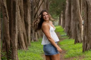 Row of tall trees creates natural pathway through green grass in outdoor portrait setting.