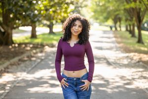 Person in purple top and jeans walks along tree-lined autumn path in natural lighting.