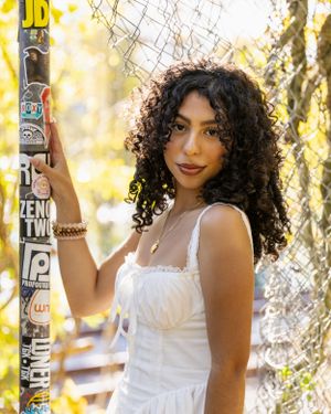 Person in white dress poses against autumn foliage with decorative bottles.