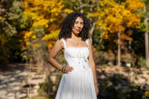 Person in white dress stands among vibrant yellow fall foliage outdoors.