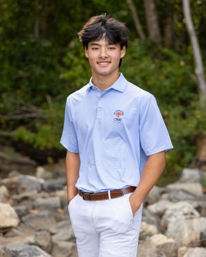 Student in light blue uniform polo and white pants poses outdoors against a rocky natural backdrop.