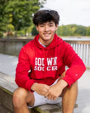 Person in red soccer hoodie sits casually on wooden bench outdoors.