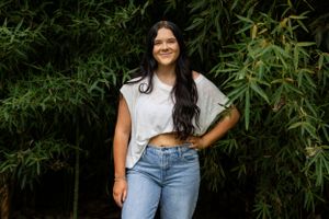 A person in casual attire poses confidently against bamboo foliage.