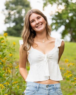 A person in a white top and jeans poses among yellow wildflowers in a garden setting.