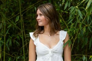 A person in a white top poses against a backdrop of green bamboo leaves.