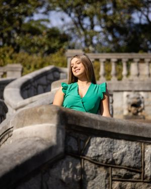 A person in a bright green dress poses on stone steps in a sunny garden setting.