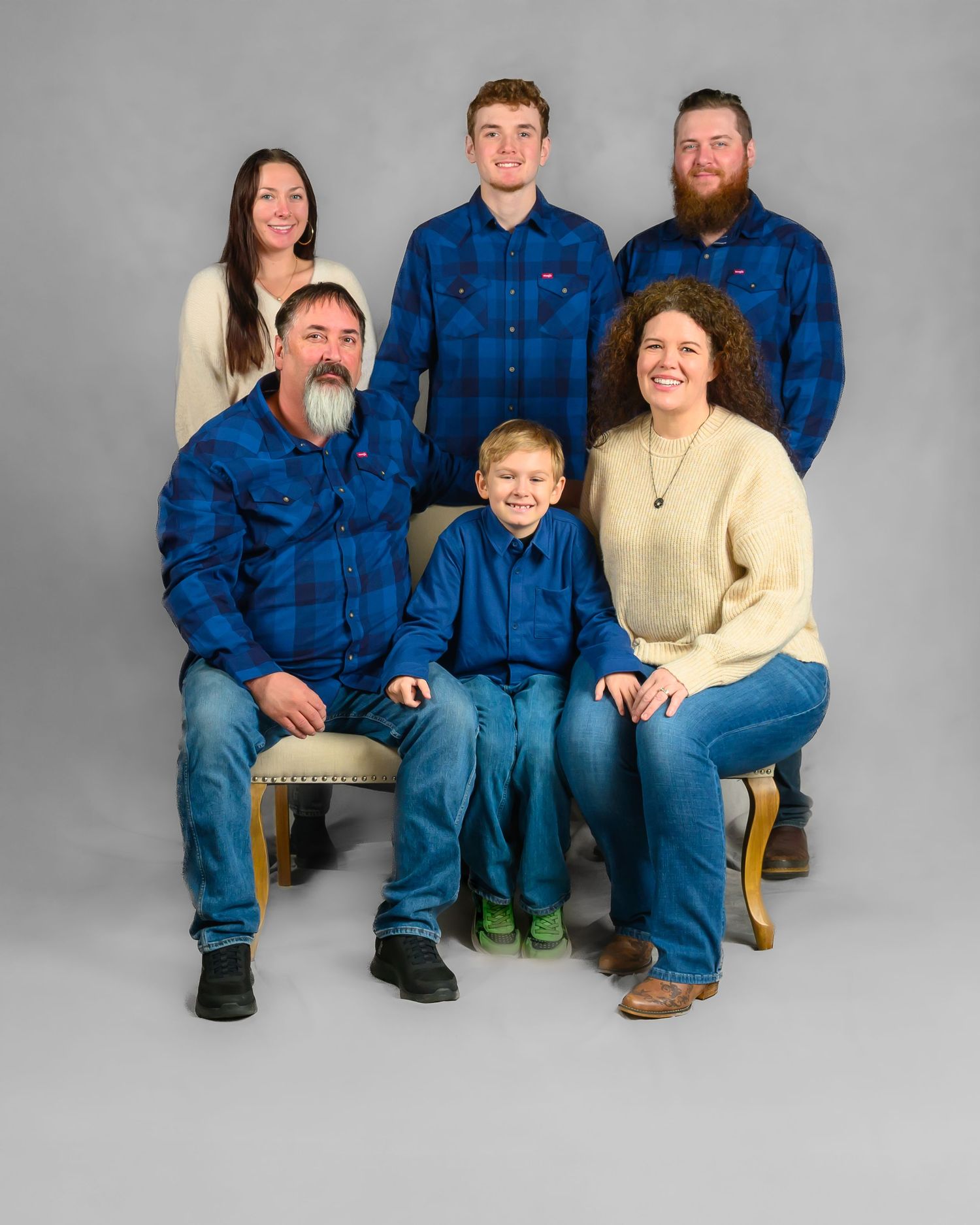 Family of six in coordinating blue flannel shirts poses for a studio portrait photo.