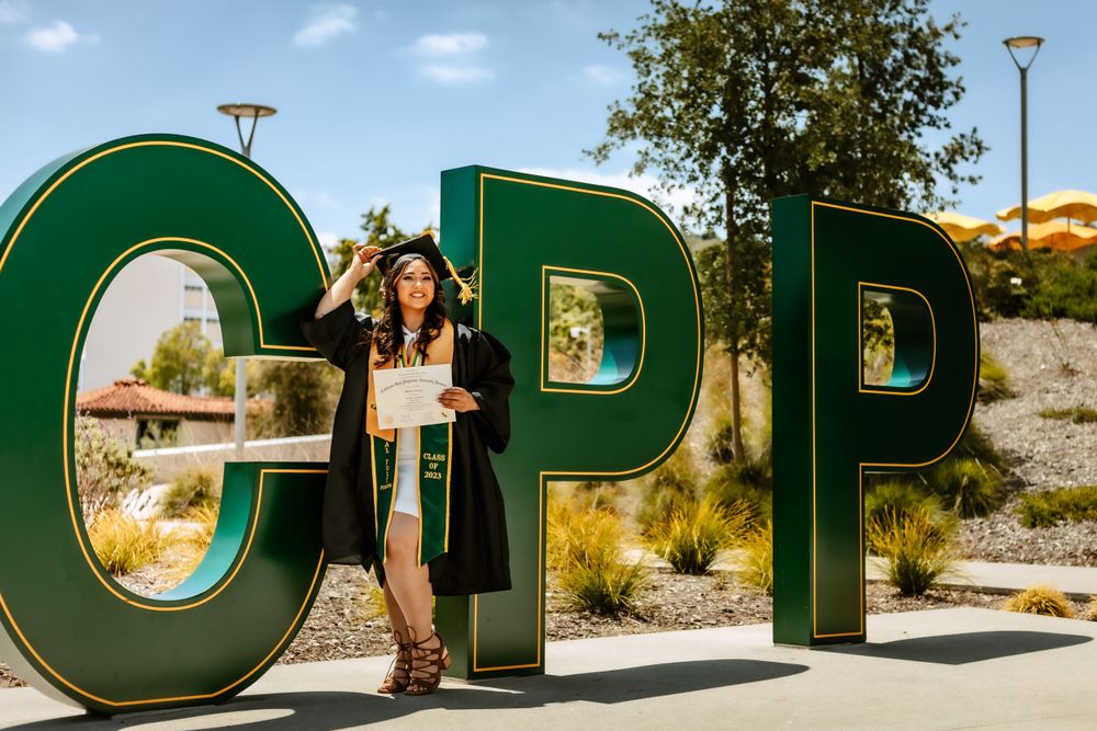 Graduate holding diploma in front of the Cal Poly Pomona sign