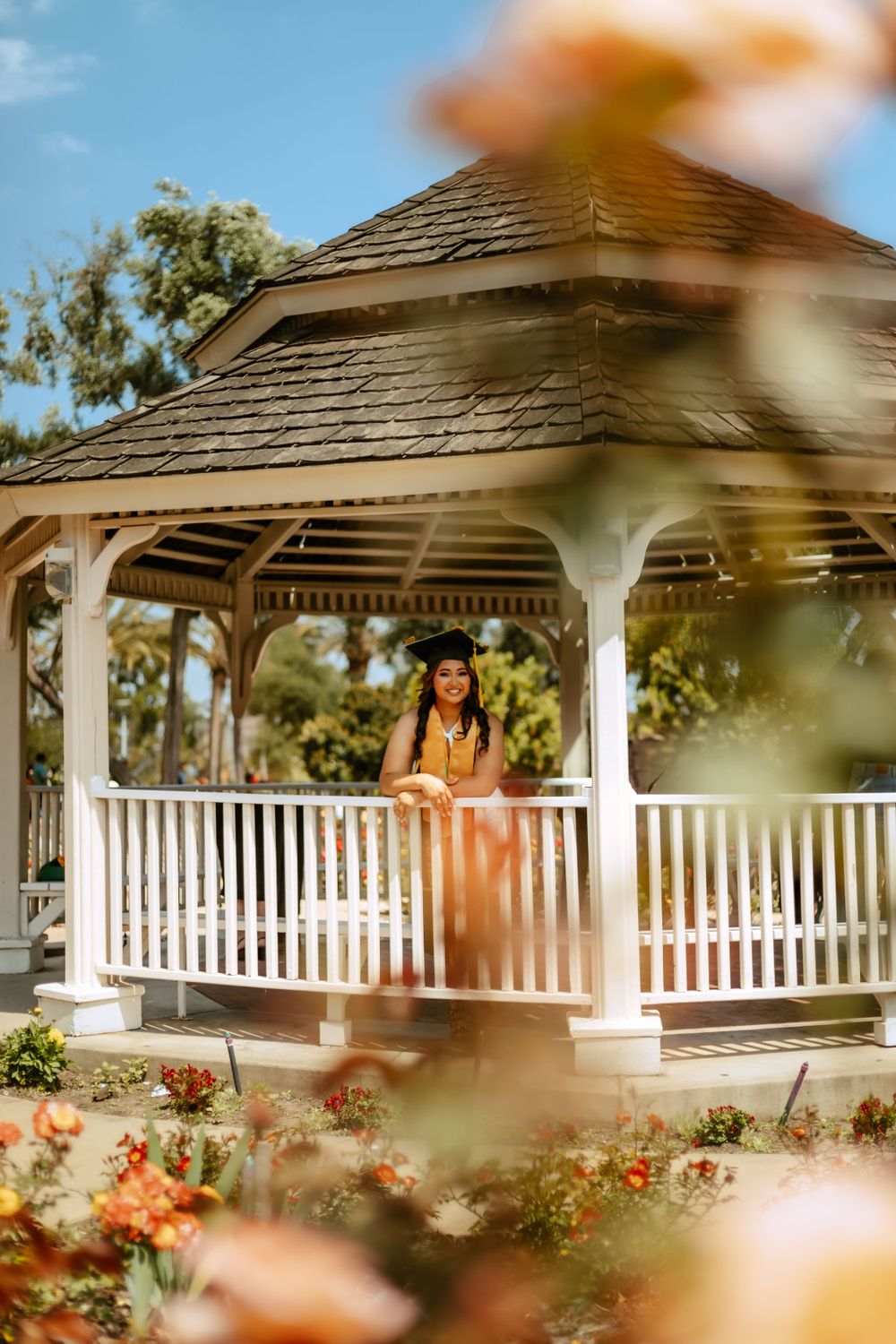 Cal Poly photograph of graduate in a white wooden gazebo surrounded by blooming flowers on a sunny day