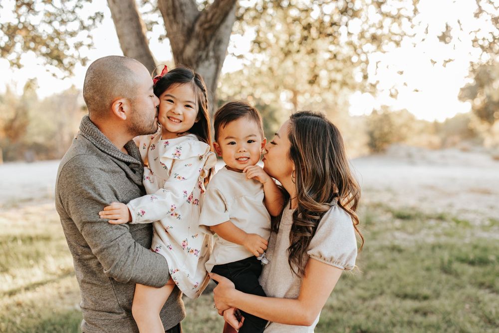 Family sharing sweet kisses with their children during outdoor portrait session.