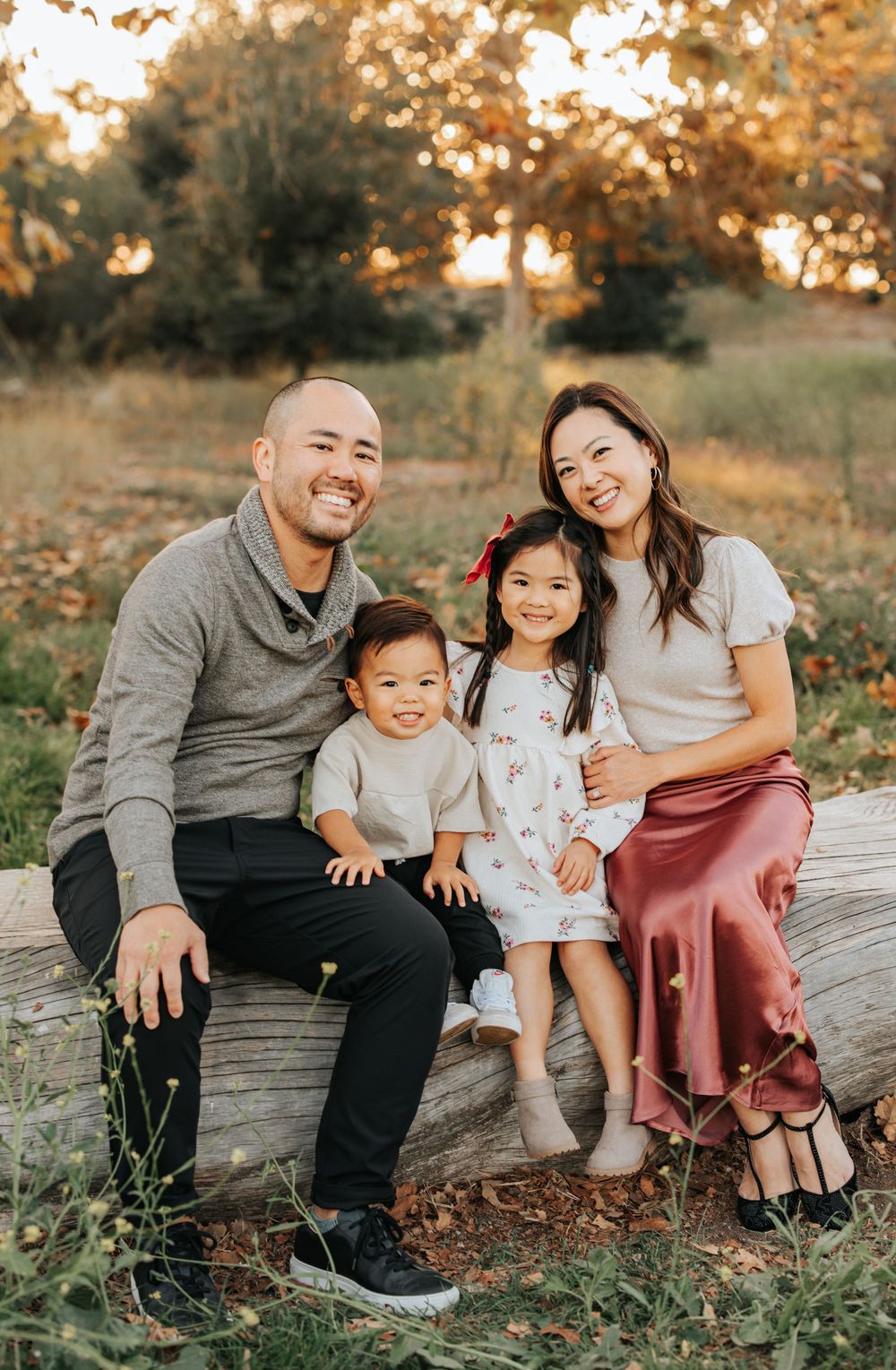 Family of four posing together on wooden bench during autumn sunset portrait session.