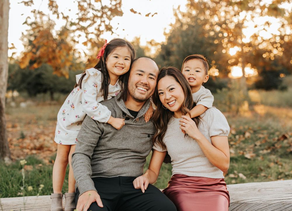 Happy family of four posing together for outdoor portrait during golden hour.