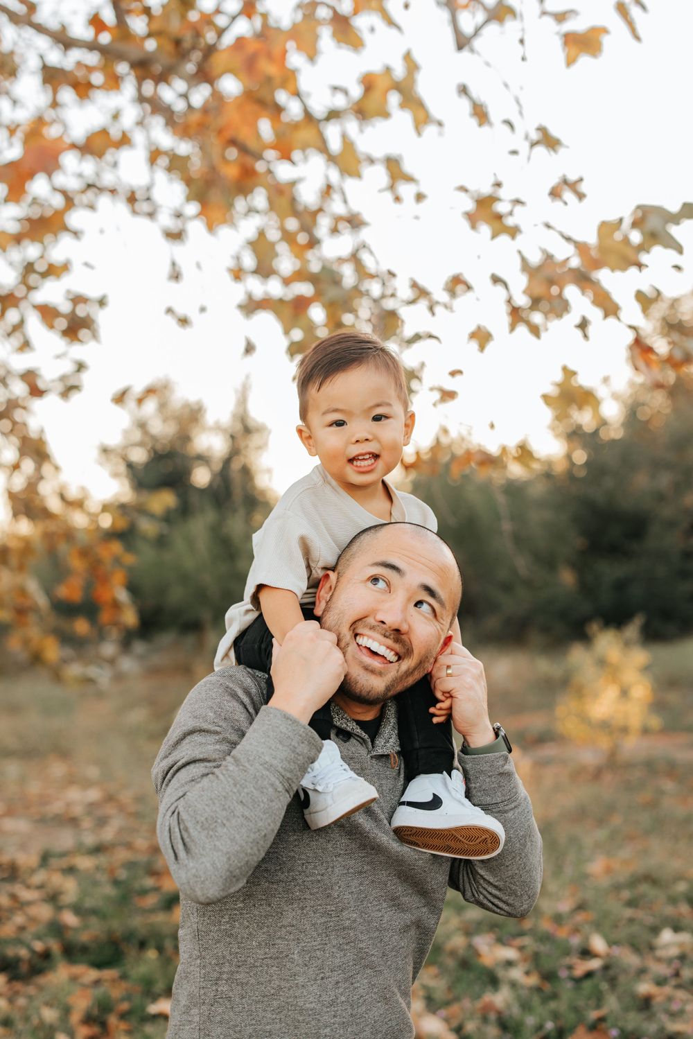Father and child sharing a joyful moment during autumn with falling leaves in the background.
