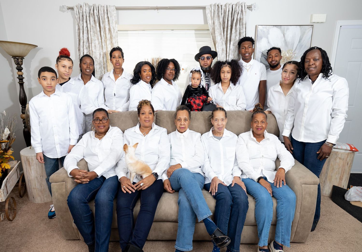 A large group photo of people wearing coordinated white shirts and jeans posed on a beige couch.