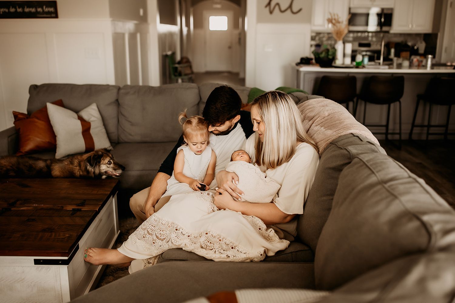 A family of four snuggle on the couch in their living room during their lifestyle newborn photoshoot.