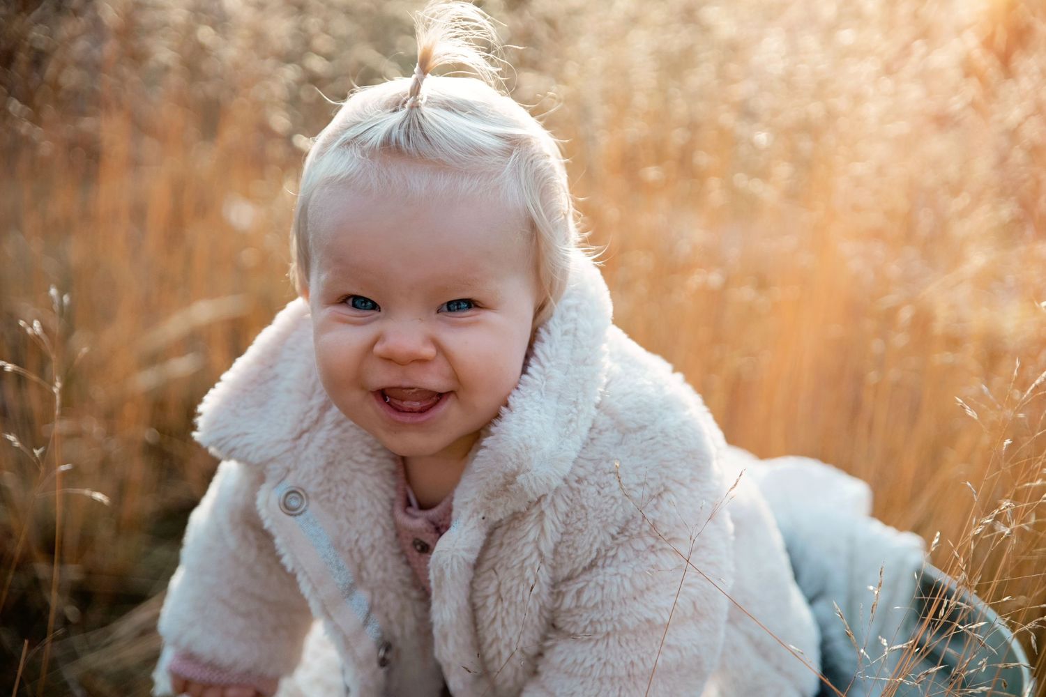 Joyful baby wearing cozy white jacket in autumn field.