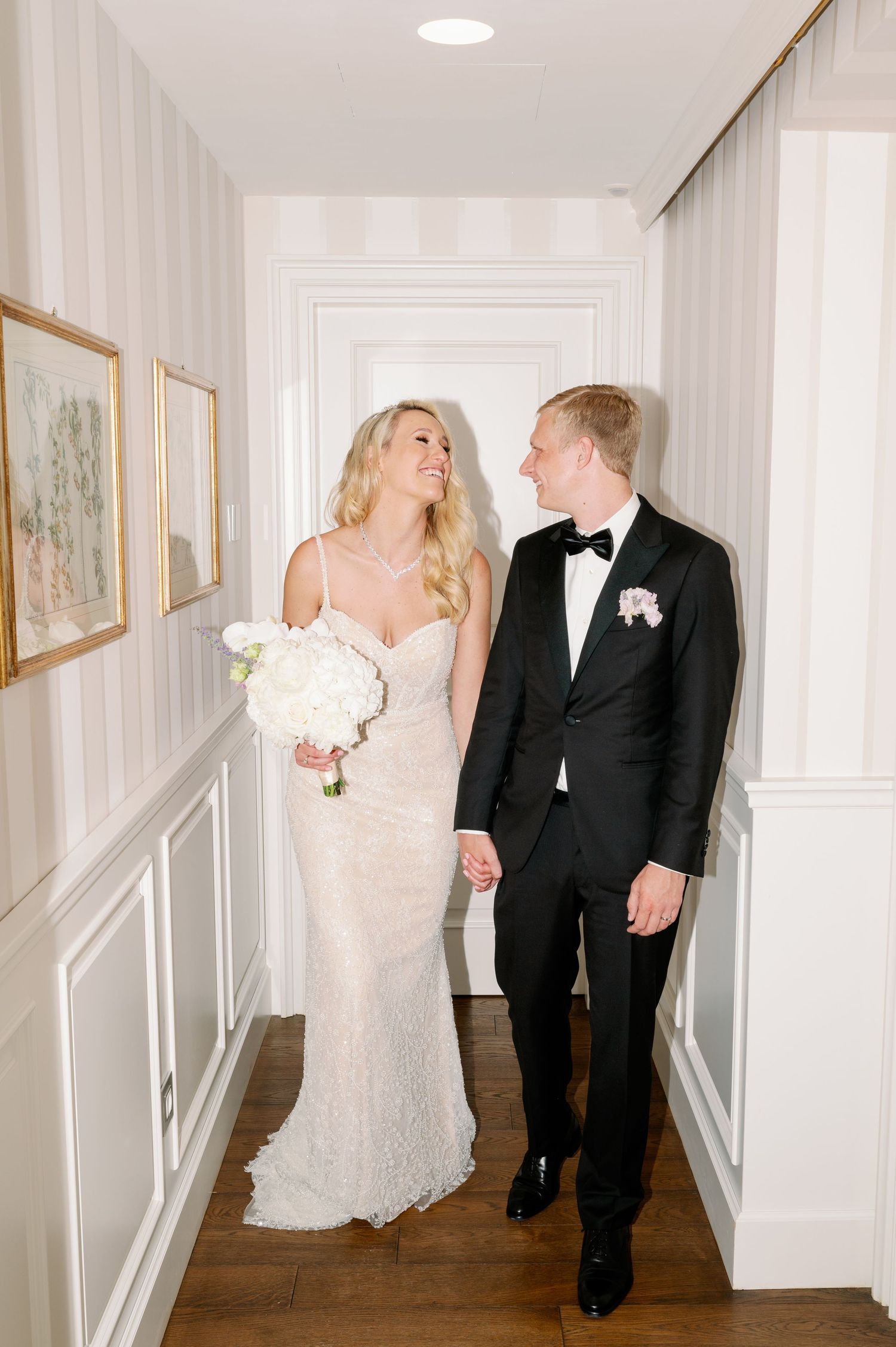 A sweet moment captured in an elegant white hallway with hardwood floors and framed artwork.