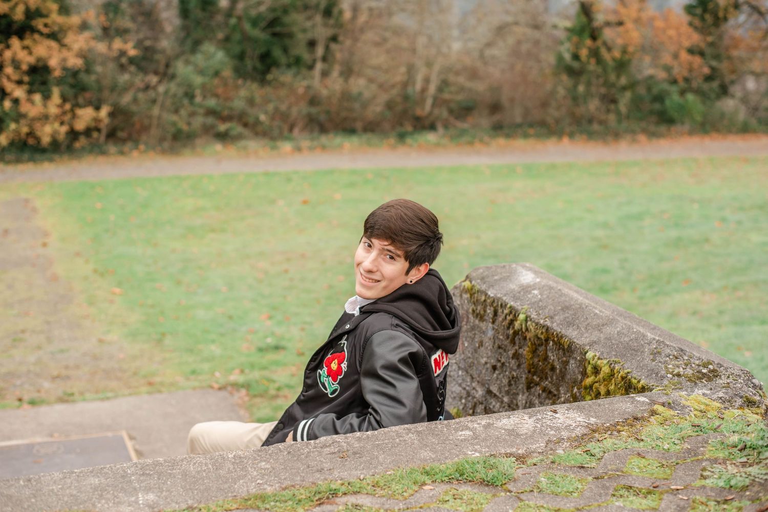 Person wearing black jacket lies on grassy slope in outdoor setting.