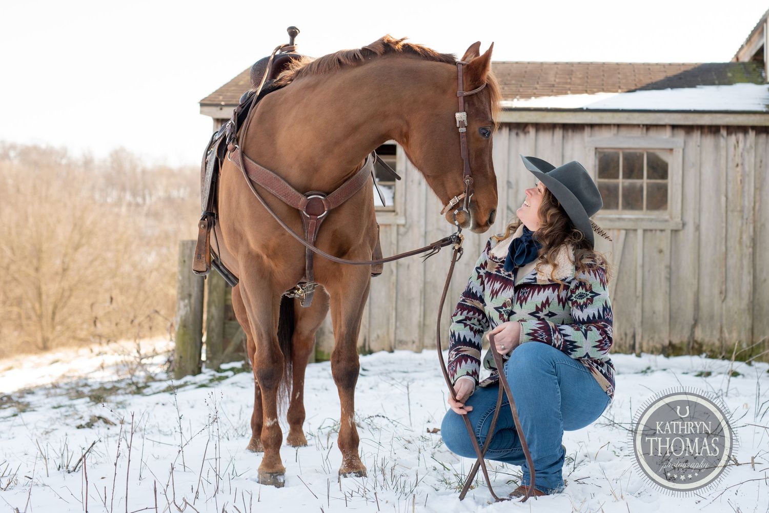 A horse and rider take a moment together in a snowy winter setting beside a rustic barn.