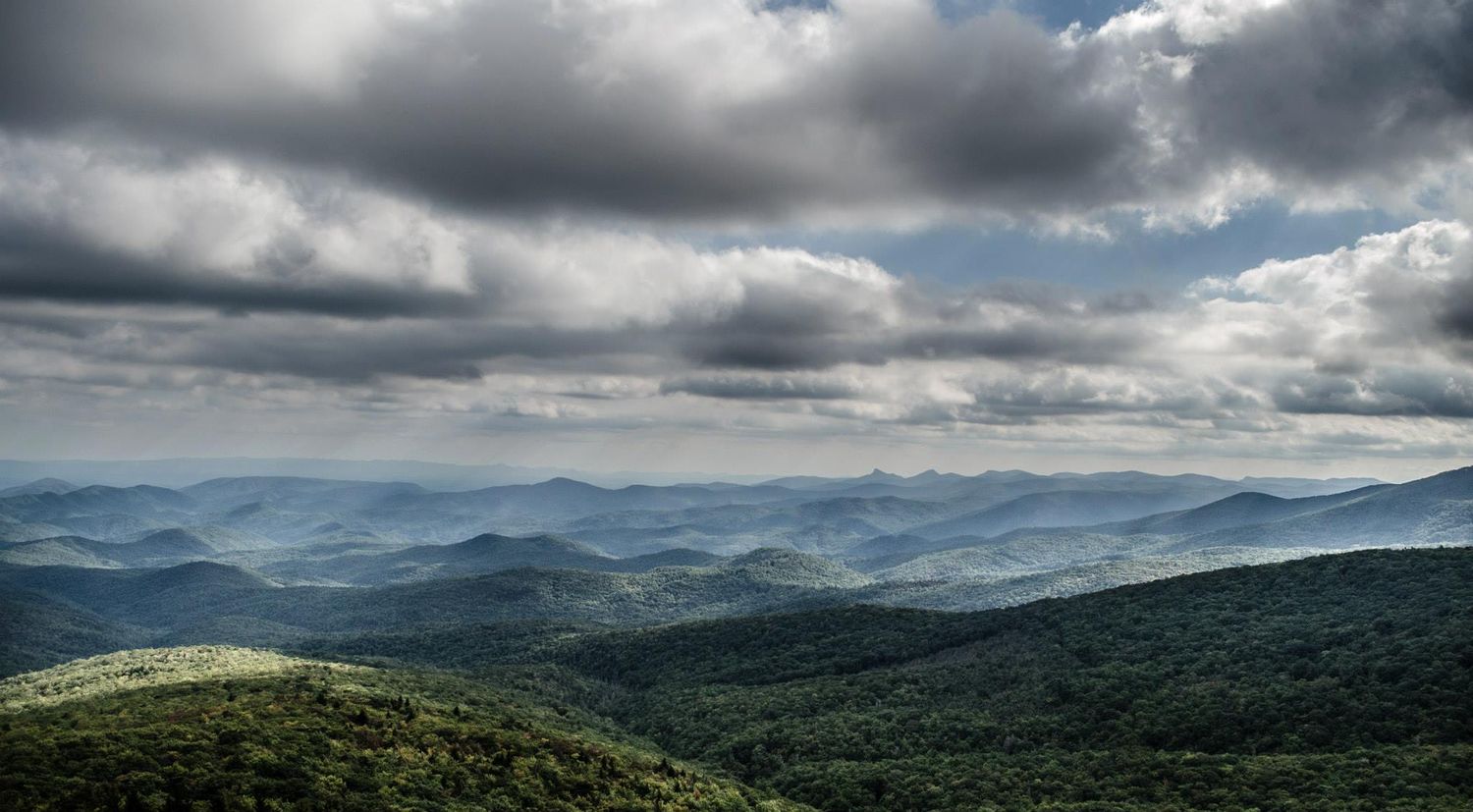 Dramatic mountain landscape with rolling hills under moody storm clouds and misty valleys stretching to the horizon.