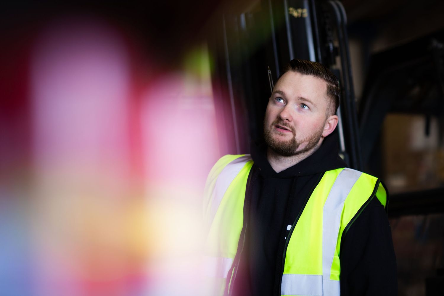 Worker wearing high-visibility vest and dark clothing in dimly lit environment.