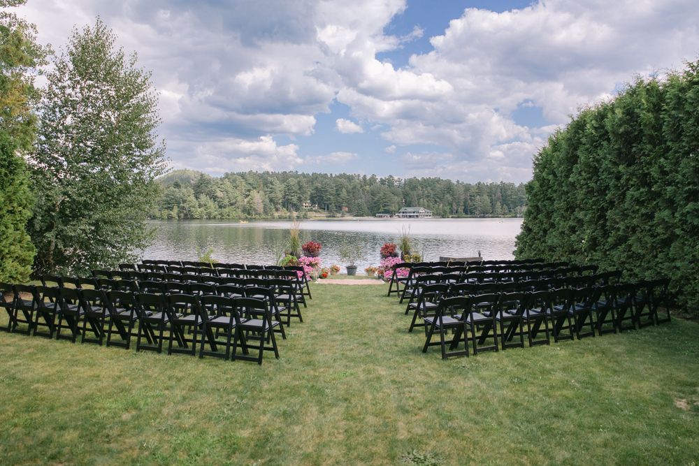 An outdoor wedding ceremony setup with black chairs facing a lakeside view.