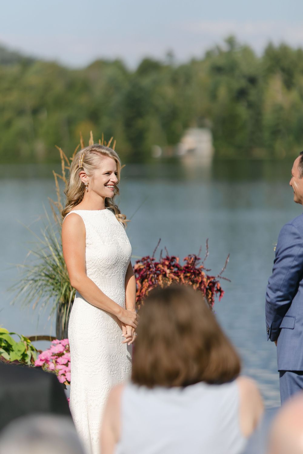A waterfront wedding ceremony with decorative grasses and pink floral arrangements.